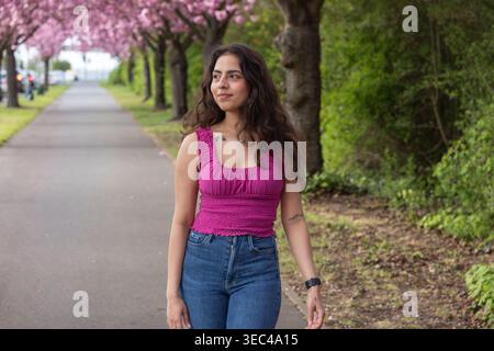Jeune femme marchant sous les cerisiers en fleurs dans le portrait de parc de printemps Banque D'Images