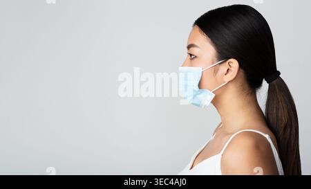 Jeune femme portant un masque de protection dans une vue de profil en gros plan sur un fond neutre Banque D'Images