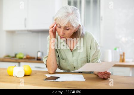 Femme mature inquiète vérifiant les papiers à la maison Banque D'Images