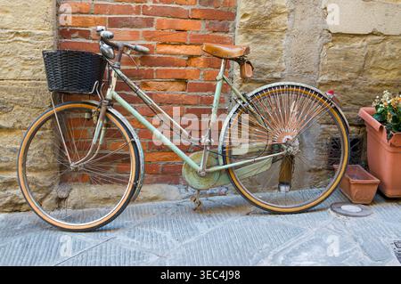 Vélo Legnano vintage avec un panier en osier garé contre un vieux mur de briques et de pierres dans une ruelle italienne pittoresque Banque D'Images