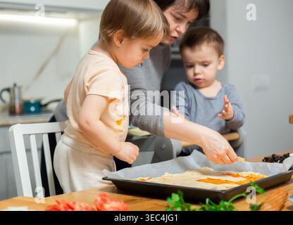 La famille cuisinent la pizza ensemble dans la cuisine à la maison confortable. Les enfants mignons avec une mère heureuse préparent la nourriture ou le repas pour le dîner Banque D'Images