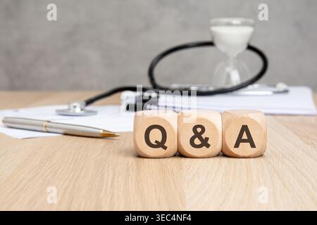 Q et Un texte sur les blocs de bois, stéthoscope, sablier et documents. Questions et réponses médicales, FAQ sur les soins de santé et concept de consultation. Banque D'Images