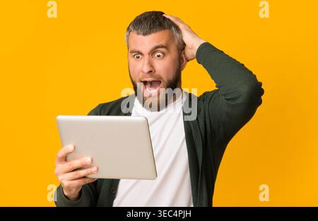 L'homme excité découvre des nouvelles surprenantes tout en utilisant Tablet sur fond jaune vif Banque D'Images
