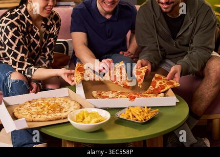 Jeunes amis adultes partageant une pizza pendant un repaire décontracté, mangeant ensemble des plats à emporter et socialisant. Idéal pour le style de vie étudiant, l'amitié, la réunion de week-end, le marketing de restauration rapide Banque D'Images
