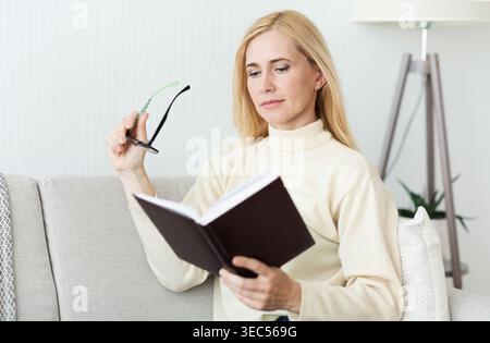Femme lisant un livre tout en étant assis confortablement sur un canapé dans un cadre confortable salon Banque D'Images