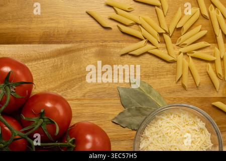 Pose à plat de tomates mûres, de pâtes Penne et de parmesan râpé sur une surface en bois Banque D'Images