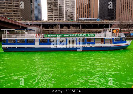 Les gens se rassemblent pour regarder la rivière Chicago tourner au vert pour la St Patricks Day. Un bateau décoré avec une bannière flotte sur l'eau vibrante pendant la célébration Banque D'Images