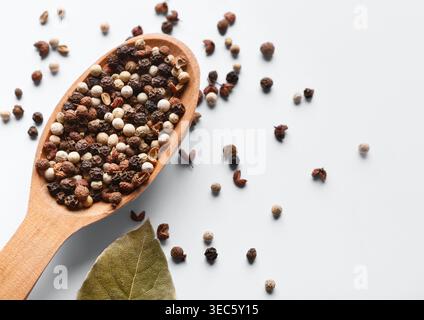 Mélange de grains de poivre dans une cuillère en bois sur fond blanc Banque D'Images