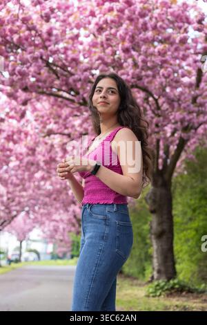Jeune femme debout sous des arbres en fleurs roses pendant le portrait de la saison de printemps Banque D'Images