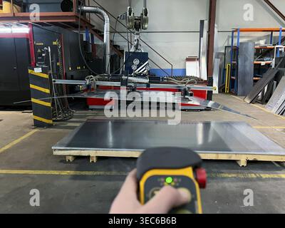 Gros plan d'un travailleur méconnaissable utilisant une télécommande pour utiliser la machine à ventouse pour transporter de grandes tôles métalliques Banque D'Images