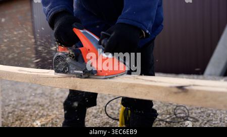 Travailleur utilisant une raboteuse électrique sur planche de bois à l'extérieur Banque D'Images