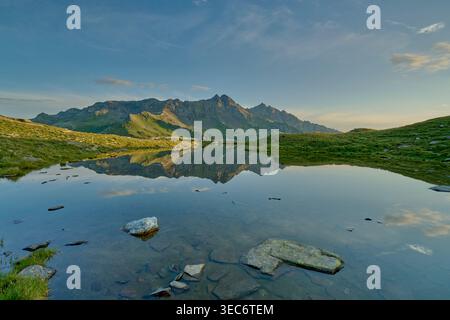 Lac alpin avec reflet clair de la chaîne de montagnes au coucher du soleil dans le Lago Bianco, Valchiavenna, Alpes italiennes, paysage pittoresque tranquille Banque D'Images