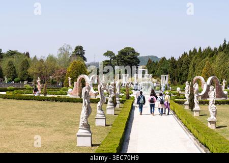 Les visiteurs se promènent le long d'un sentier ensoleillé bordé de statues blanches classiques et de haies bien entretenues, menant à une grande fontaine centrale et élégante Banque D'Images