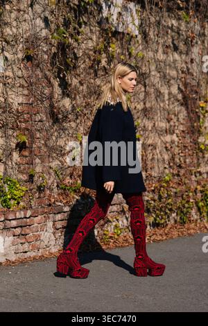 Milan, Italie - 24.09.2021, Natalia Verza porte un manteau noir surdimensionné associé à des bottes à plateforme Prada à motifs rouges. Style de rue Prada Banque D'Images