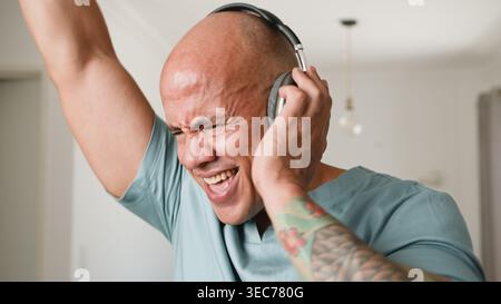 Joyeux homme tatoué chantant et écoutant de la musique sur des écouteurs à la maison Banque D'Images