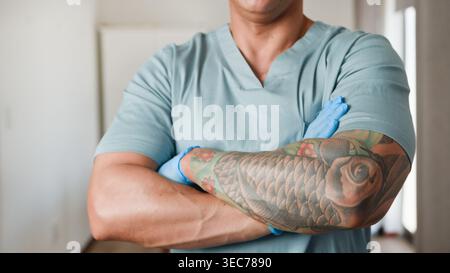 Professionnel de la santé confiant avec bras tatoué en gommages et gants montrant force et soin Banque D'Images