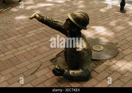 Sculpture ouvrière en bronze émergeant du trottoir à Subotica, Serbie. Art public ludique et détail de rue urbaine dans le centre-ville. Banque D'Images