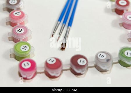 Fournitures d'art, y compris des récipients de peinture et des pinceaux disposés soigneusement sur une surface blanche. Différentes couleurs sont visibles dans les petits conteneurs Banque D'Images