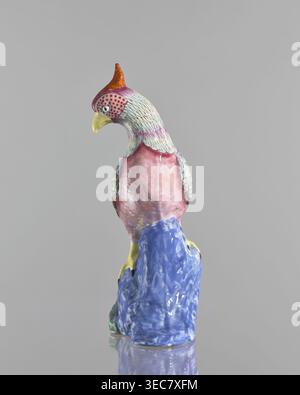 Figurine de coq, chinoise, Qing 1644–1911, XIXe siècle. Sculpture en porcelaine colorée d'un coq avec des rochers ; hauteur 28,5 cm, largeur 14,0 cm. Figurine animale en céramique., sculpture d'oiseau en céramique perchée sur une base sculptée, représentée sur un fond gris Uni. L'oiseau a une crête orange et rouge, un bec jaune, et une tête avec des plumes verdâtres pâles et des zones de motifs rouges pointillés près de l'œil. Le cou et le haut de la poitrine montrent des plumes verdâtres pâles passant aux tons rose et rouge sur le corps, avec des plumes texturées des ailes en vert pâle et gris. La base sous l'oiseau est bleu brillant Banque D'Images