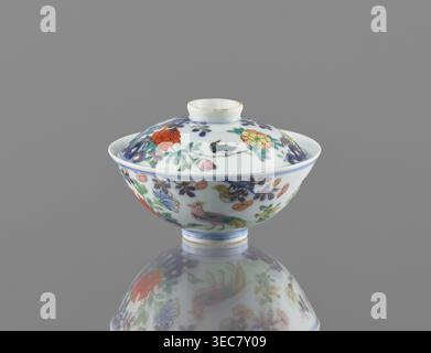 Bol avec couvercle, chinois, dynastie Qing, période Qianlong 1736–1795. Récipient en porcelaine colorée décoré dans un jardin avec des rochers, des arbres, des pivoines, des magnolias, des chrysanthèmes; deux faisans et un papillon. Signé. Hauteur 7,5 cm ; diamètre 11,7 cm ; poids 0,2 kg., Un bol en porcelaine à couvercle avec un pied arrondi se trouve sur une surface réfléchissante, montrant une image miroir en dessous ; le bol et le couvercle sont blancs avec des motifs floraux peints et oiseaux dans des couleurs incluant rouge, jaune, vert, bleu, violet, rose et orange, et il y a des zones de bordure dorée ou brunâtre ; l'arrière-plan est un gris uniforme. Banque D'Images