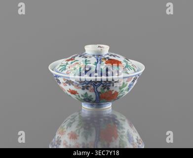 Bol avec couvercle, chinois, dynastie Qing, période Qianlong 1736–1795. Récipient en porcelaine colorée, hauteur 7,5 cm, diamètre 11,7 cm, poids 0,2 kg. Décoration : dans un jardin serti de rochers, arbres, pivoines, magnolias, chrysanthèmes deux faisans et un papillon. Signé., Un petit bol en porcelaine à couvercle repose sur une surface réfléchissante sur un fond gris Uni, montrant un motif décoratif de motifs floraux et botaniques dans des couleurs incluant blanc, bleu, vert, rouge, orange, rose, et or ; le bol a une forme arrondie avec un pied court et un couvercle bombé surmonté d'un petit bouton, et les motifs peints Banque D'Images