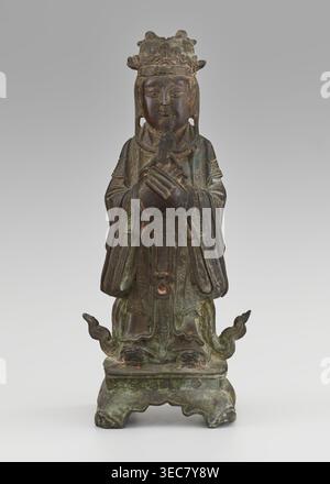 Dignitaire — officiel ; fabricant, figurine d'un homme ; art chinois ; culture : chinois ; sujet : savants, sages, fonctionnaires du gouvernement ; matériau : sculpture ; date : dynastie Qing du XIXe siècle, 1644–1911 ; dimensions : hauteur 28,5 cm, largeur 12,4 cm, profondeur 8,7 cm., Une statue debout altérée avec une patine de tons vert, brun et bronze foncé représente une figure rodée portant une couronne ornée, tenant un petit objet avec les deux mains croisées au niveau de la poitrine ; le visage est serein avec des lèvres fermées et des traits faciaux fins sculptés, et de longs rabats d'oreilles ou des cheveux pendent à côté du visage. Les robes coulantes s'affichent en détail Banque D'Images