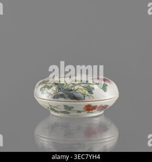 Boîte à couvercle, chinoise, porcelaine colorée décorée de grenades, chrysanthèmes et pivoines, ornements floraux ; milieu du XIXe siècle dynastie Qing, 1644–1911 ; récipient en céramique pour instruments d'écriture ; hauteur 3,2 cm, diamètre 7,9 cm., Une petite boîte ovale en porcelaine avec un couvercle bombé repose sur un fond gris Uni, sa surface principalement blanche avec des motifs botaniques peints en vert, bleu, violet, rouge, rose, et orange, montrant des feuilles, des fleurs et une forme rocheuse bleuâtre ; la boîte a un bord mince de couleur or où le couvercle rencontre la base et repose sur une surface grise réfléchissante qui crée un miroir doux Banque D'Images