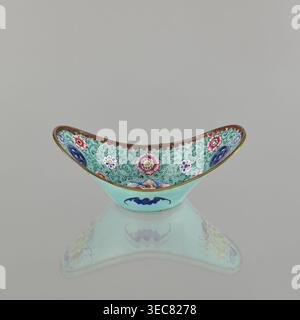 Bol, émail peint, Qing 1644–1911, chinois, XVIIIe/XIXe siècle. Récipient en céramique orné de lotus, pièces de monnaie, tendres de fleurs et iconographie de chauves-souris symbolisant le bonheur. Hauteur 6,3 cm ; largeur 8,5 cm ; profondeur 15,3 cm., un bol ornemental en forme de croissant incurvé repose sur une surface réfléchissante, montrant un dessous en miroir ; l'extérieur du bol est un turquoise clair avec un motif stylisé bleu foncé, tandis que l'intérieur présente un fond à motifs détaillés en turquoise avec des tourbillons ornés et une bordure en rouge brunâtre, décoré de médaillons floraux en rose, blanc, bleu et jaune Banque D'Images