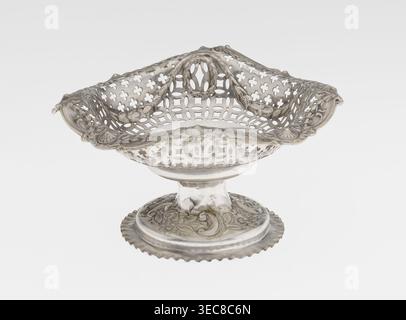 Stand de gâteau ajouré par Mappin & Webb Ltd Goldsmith, plier, vendeurs ; fl. 1859-. Support de gâteau ajouré sur une base circulaire avec un rebord, surélevé et décoré en relief avec des motifs rocaille et floraux. La tige courte supporte un bol circulaire passant en carré avec des bords retournés et arrondis, décoré d'ovales, de festons, de couronnes et de rosettes. Matériaux/technique : ajouré, décoration en relief. Date : 1903/1904. Lieu : Londres, Angleterre. Type d'objet : vaisseau. Dimensions : hauteur 7,2 cm ; largeur 14,3 cm ; profondeur 14,3 cm ; poids 112 g., Un bol décoratif en métal avec un motif de treillis percé orné et Banque D'Images