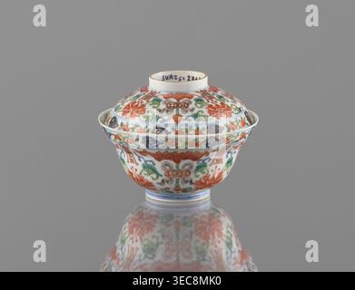 Bol avec couvercle ; porcelaine de couleur chinoise, dynastie Qing (période Qianlong, 1736-1795), décoré de chauves-souris, shou de longévité, ornement tendon de lotus, lotus et pêches ; navire ; hauteur 9 cm, diamètre 10,7 cm, un petit bol en porcelaine à couvercle est centré sur un fond gris Uni, décoré partout de motifs floraux et foliés complexes en rouge, vert, bleu et touches de brun sur un fond blanc ; le couvercle et le bol affichent des motifs ornementaux répétés comprenant des fleurs stylisées et des feuilles défilantes, et la pièce repose sur un pied court avec des bandes bleues concentriques, sa surface peinte Banque D'Images
