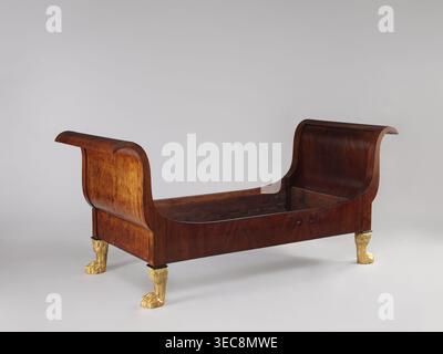 Lit avec fronces en forme de S incurvées vers l'extérieur de même hauteur et planches latérales droites, soutenu par quatre pattes sculptées et dorées en forme de pattes d'animaux à fourrure. Acajou, avec des frontaux de cadre ayant des panneaux simples, de forts retournements en haut et des fonds simples, reliés aux côtés avec des vis et des crochets. Les coins supérieurs des côtés s'arquent dans les cadres de fronton ; le fond intérieur est muni de bandes dentées collées soutenant les lattes transversales sous le matelas. Un fronton plaqué à l'extérieur avec de l'acajou teinté de cendre. Style Empire, 1815-1830, Varsovie, Europe centrale. Dimensions : hauteur 103 cm, largeur 192 Banque D'Images