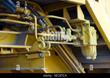 Un réseau complexe de lignes hydrauliques industrielles et de raccords métalliques jaunes sur les machines lourdes. Banque D'Images