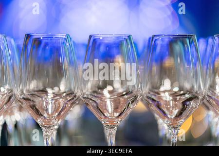 Élégant stand de verres à vin vides disposés sur une table, reflétant des lumières bokeh bleues et dorées en arrière-plan. Prêt pour l'événement Banque D'Images