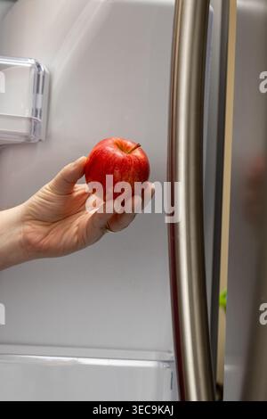Gros plan vertical de la main prenant Red Apple de la porte du réfrigérateur à la maison Banque D'Images