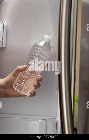 Gros plan vertical de la main prenant une bouteille d'eau du réfrigérateur à la maison Banque D'Images
