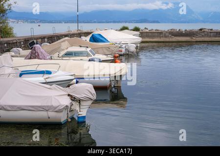 Rangée de petits bateaux recouverts de bâches amarrées dans le port calme, avec lac pittoresque et montagnes en arrière-plan, scène de paysage paisible en front de mer. Banque D'Images