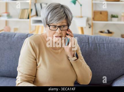 Femme âgée à la maison assise sur un canapé, écoutant attentivement pendant un appel téléphonique Banque D'Images