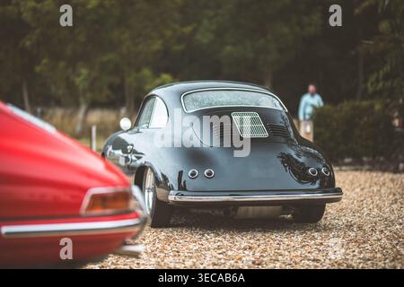 Une voiture de sport noire vintage est garée sur une allée de gravier, avec une voiture de sport rouge devant Banque D'Images