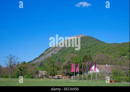 Visegrad, Hongrie - 18 avril 2026 : vue large du Haut Château sur une colline avec des drapeaux de la ville au premier plan sous un ciel bleu clair avec un nuage. Banque D'Images