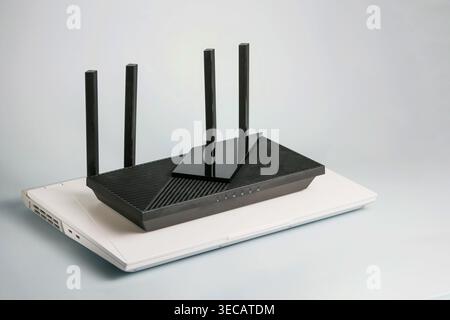 Routeur Wi-Fi noir avec quatre antennes placées sur un ordinateur portable blanc. Réseau domestique moderne, connectivité Internet et concept de configuration technologique sur BA blanc Banque D'Images
