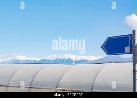 Panneau directionnel bleu vierge contre les sommets enneigés des montagnes Banque D'Images