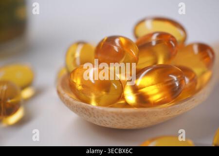 Beaucoup de capsules d'huile de poisson sur une cuillère en bois sur une surface légère Banque D'Images