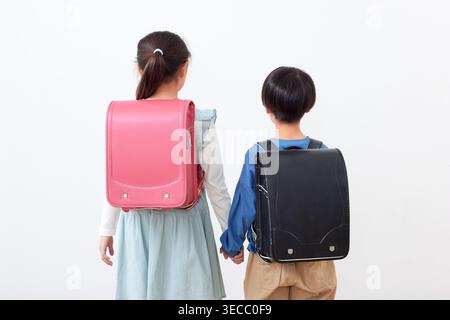 Frères et sœurs de l'école primaire japonaise tenant la main portant le randoseru rose et noir studio de vue arrière Banque D'Images