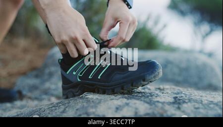 Personne, mains et attacher avec des chaussures pour l'aventure de randonnée, le fitness ou la préparation sur le rocher dans la nature. Randonneur, touriste ou se préparer avec des lacets ou Banque D'Images