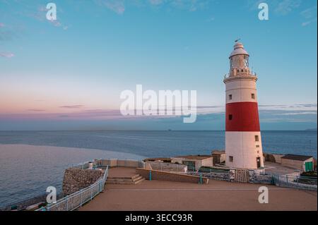 Un phare frappant avec une bande rouge et blanche se dresse à Europa point à Gibraltar, surplombant la mer tranquille pendant le coucher du soleil. La scène comporte un Banque D'Images