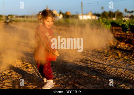 Fille jouant avec la terre dans la lumière chaude de coucher de soleil Banque D'Images