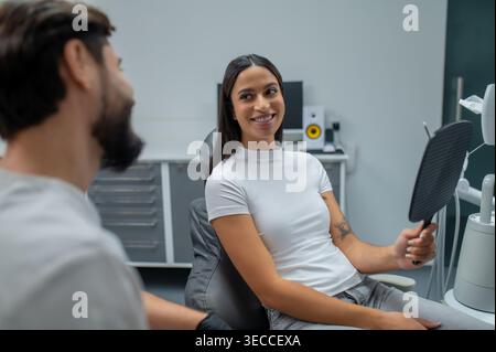 Patiente contente regardant le miroir sur les résultats du travail des dentistes Banque D'Images