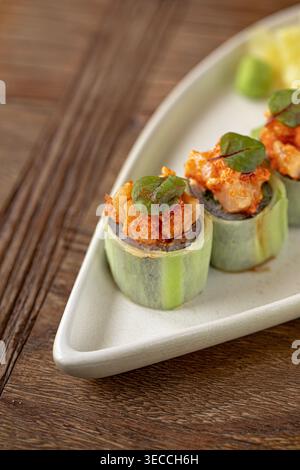 Rouleaux de sushi enveloppés dans du concombre avec garniture épicée Banque D'Images