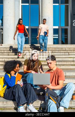 Étudiants divers collaborant sur ordinateur portable dans les escaliers du campus Banque D'Images