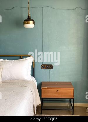 Détail intérieur minimaliste de la chambre avec lit, table de chevet en bois et lampe suspendue sur le mur bleu texturé Banque D'Images
